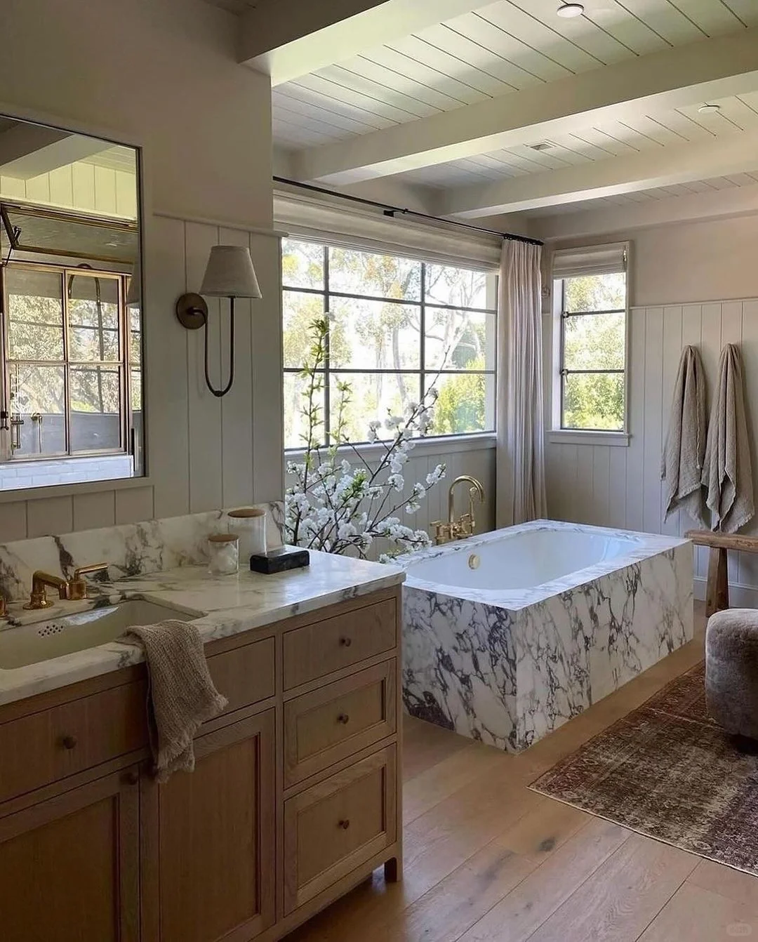 Modern bathroom with large windows, marble bathtub, light curtains, and wood vanity.