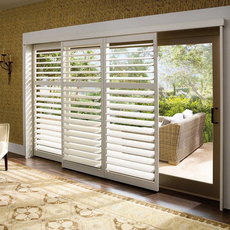 White sliding plantation shutters on glass doors, opening to a patio with outdoor wicker furniture