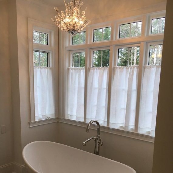 Bright bathroom with sheer white cafe curtains, freestanding tub, and modern chandelier