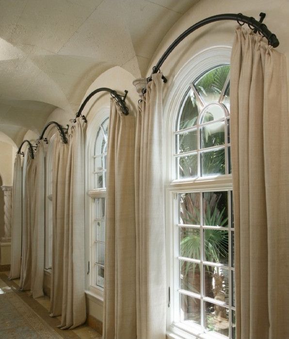 Beige blackout curtains on curved track system framing arched windows in a bright hallway.