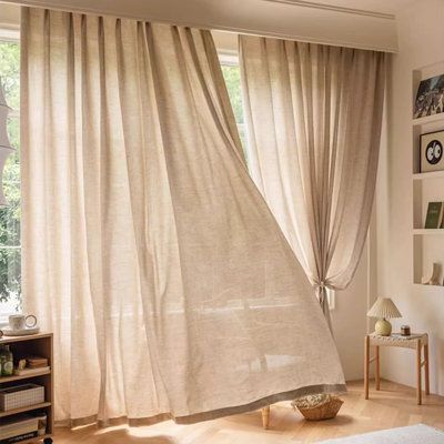 Beige sheer curtains on modern curtain track in sunlit living room with wood floor and cozy decor