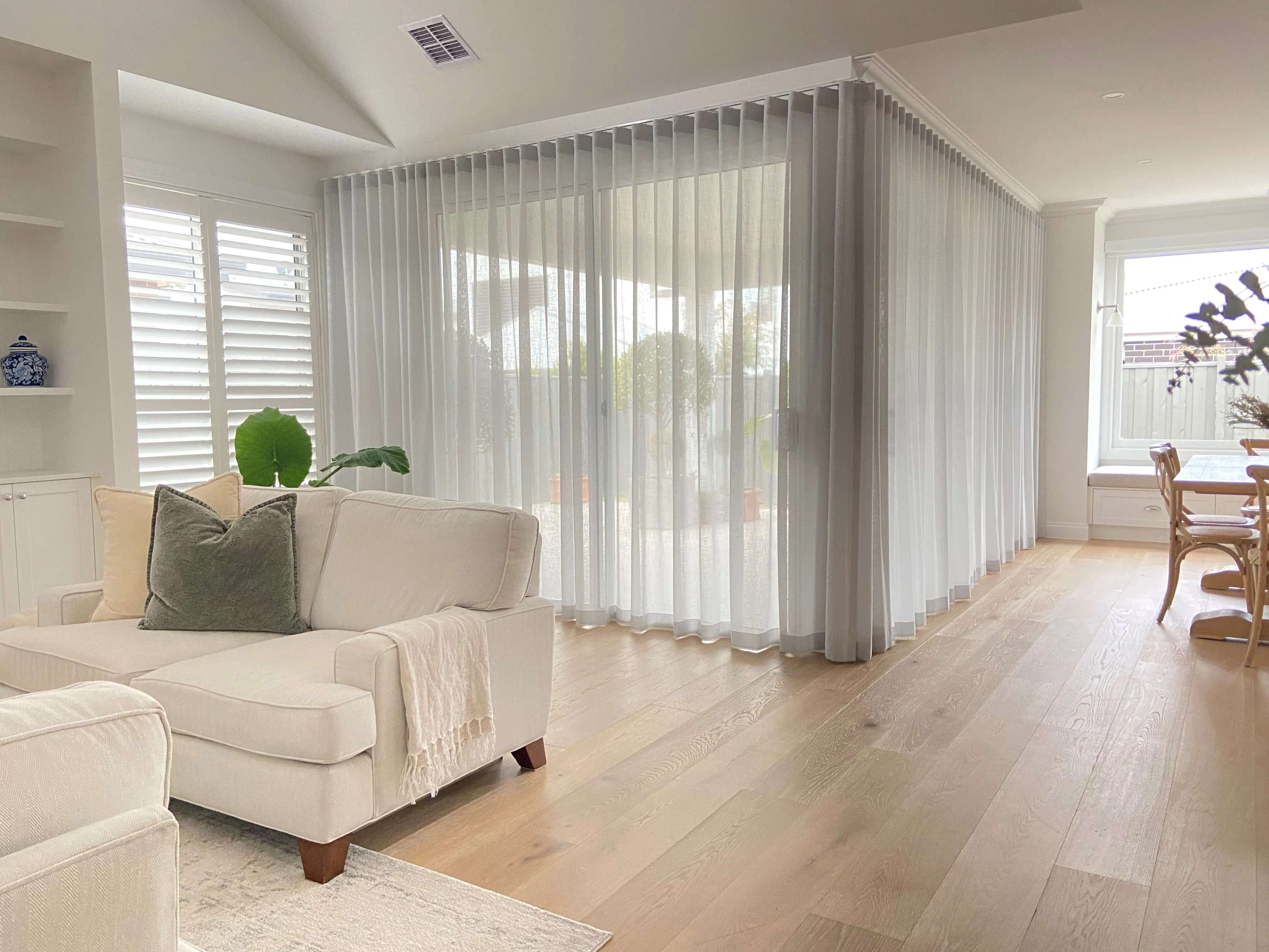Modern living and dining area with sheer floor-to-ceiling curtain tracks and light wood flooring