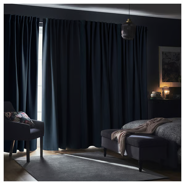 Dark blackout curtains in a cozy modern bedroom with bed, chair, and soft lighting