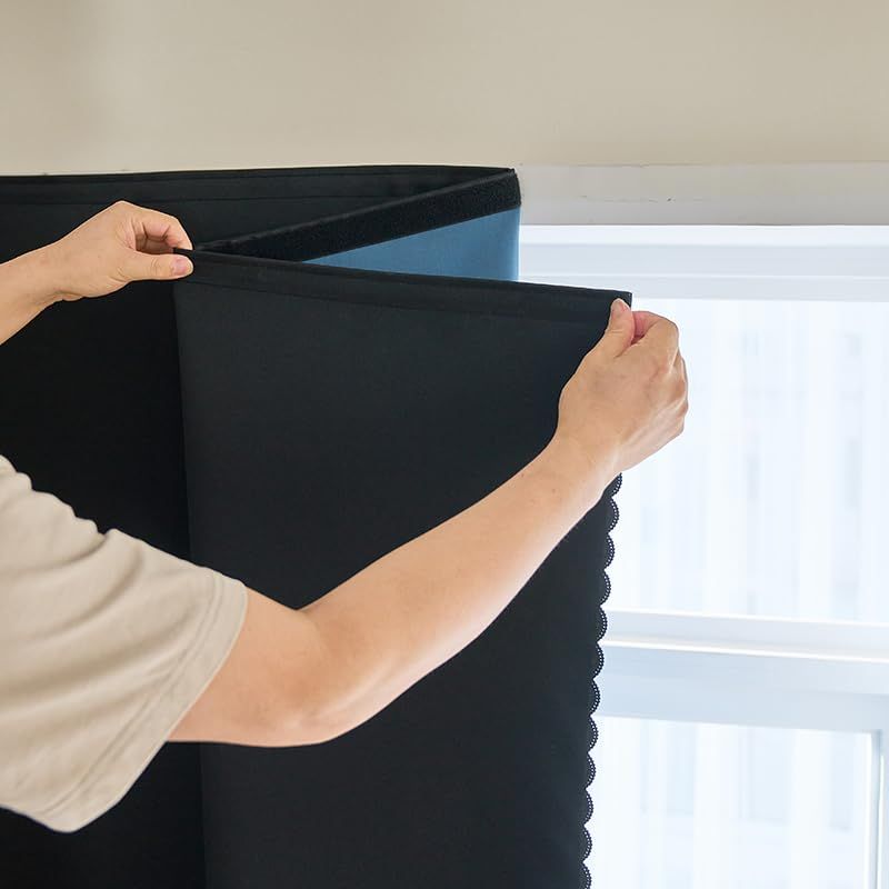 Person installing black blackout curtain panel on a window with scalloped edge design.