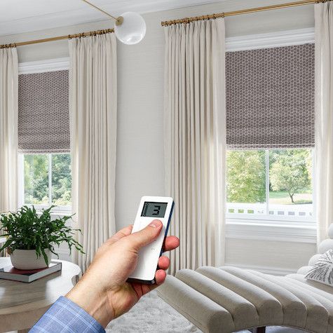 Hand holding remote controls automated thermal blackout curtains in modern living room