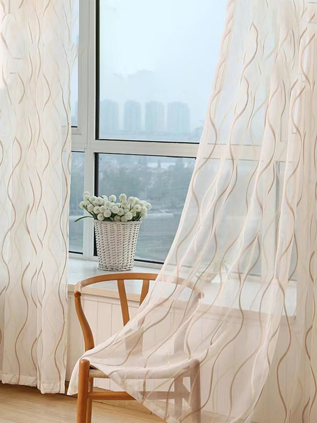Sheer wavy-pattern curtains by a bright window, wooden chair, and white flower vase