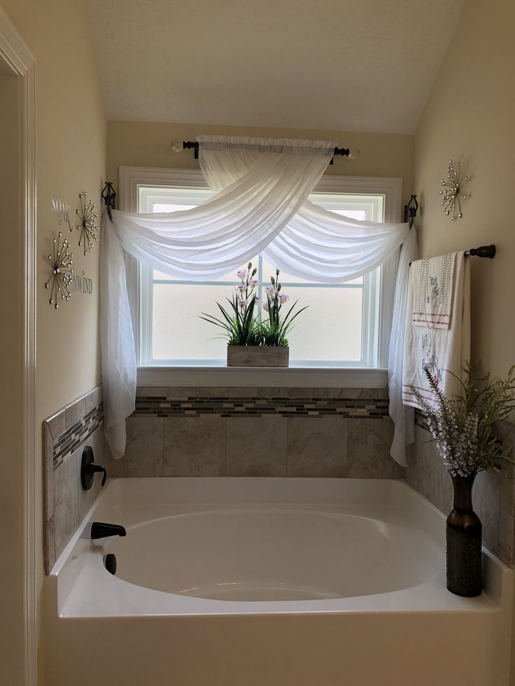 Elegant bathroom with white sheer curtains on window, above soaking tub and potted plant decor