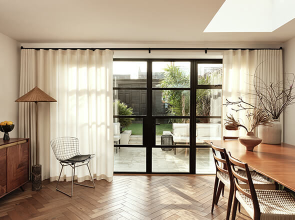 Modern living room with sheer curtain panels on a black curtain track system, large glass doors opening to a patio, and stylish wooden furniture.