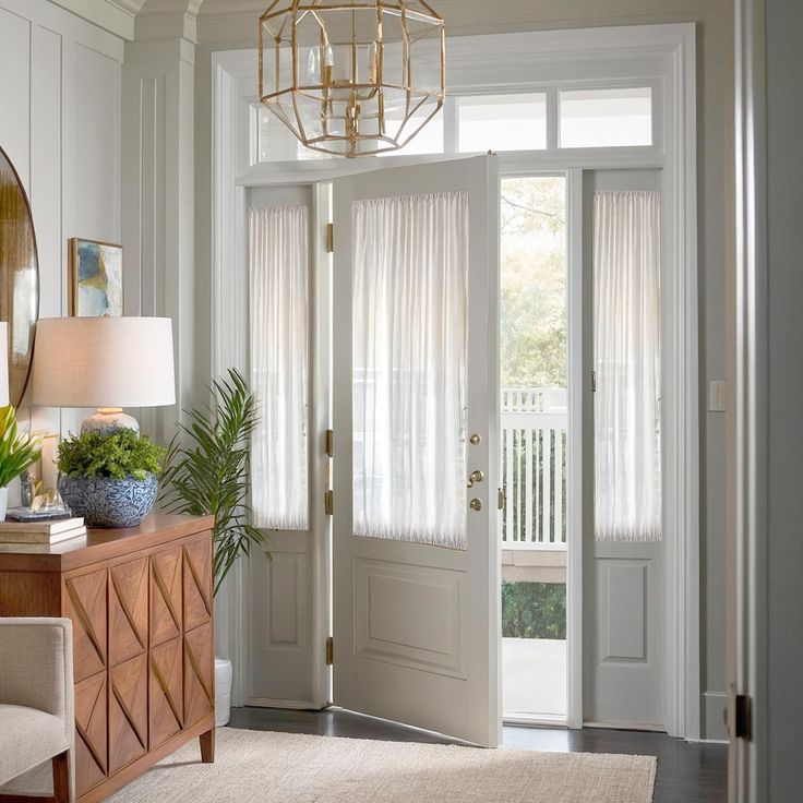 Bright entryway with sheer white curtains on French doors, modern chandelier, and wooden console table.