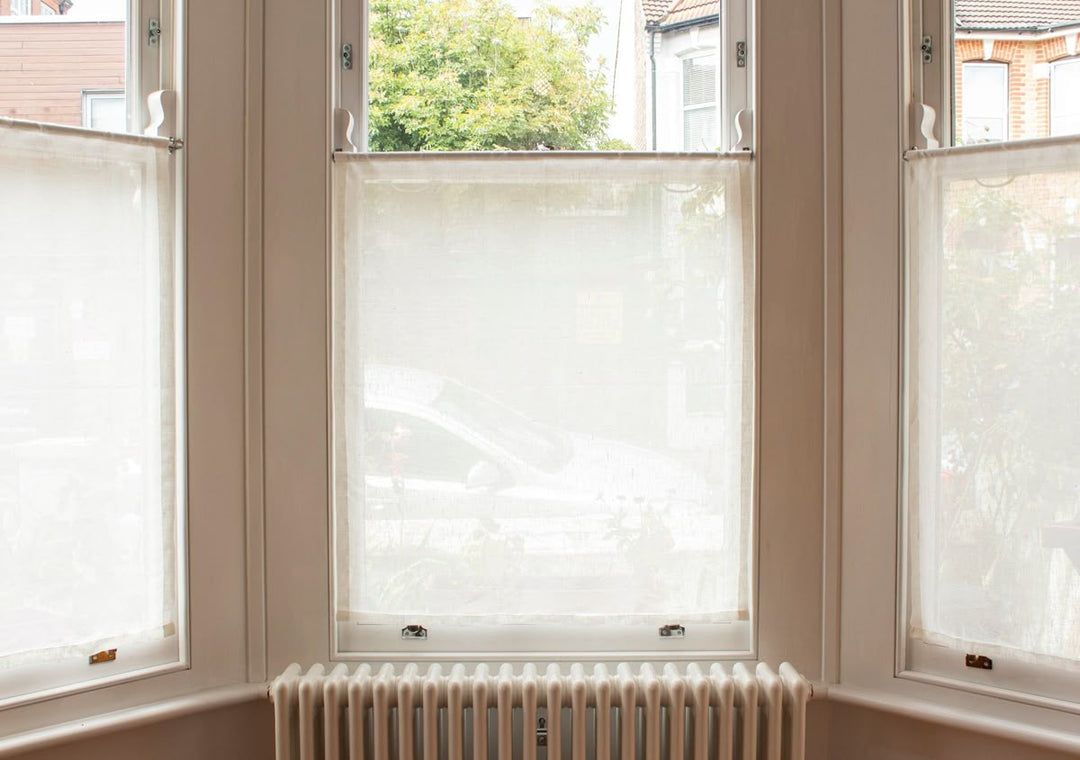 Bright bay window with sheer white curtain panels and a radiator below.
