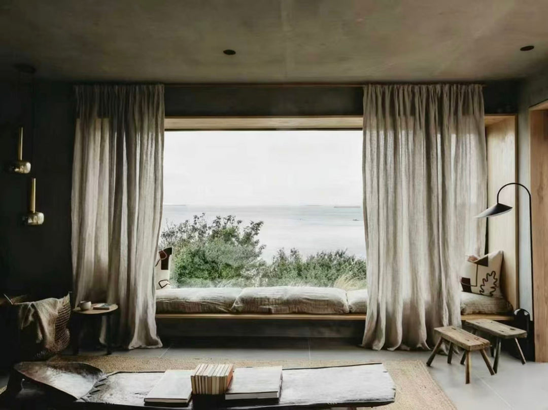 Cozy living room with large floor-to-ceiling window, neutral curtains, window seat, and sea view