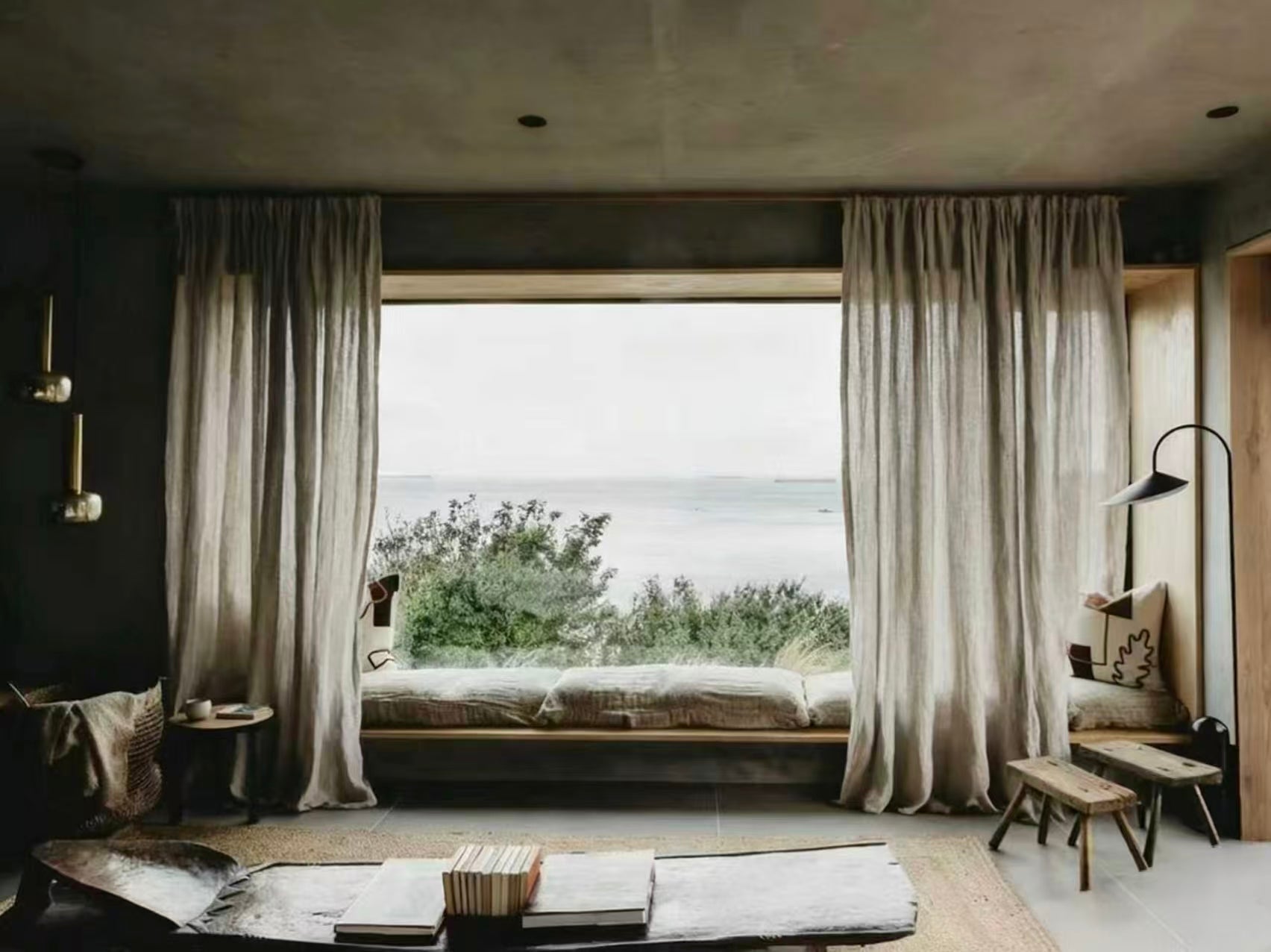 Cozy living room with large floor-to-ceiling window, neutral curtains, window seat, and sea view