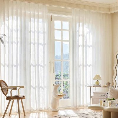 Bright living room with sheer white curtains, large windows, and bear-shaped decor statue