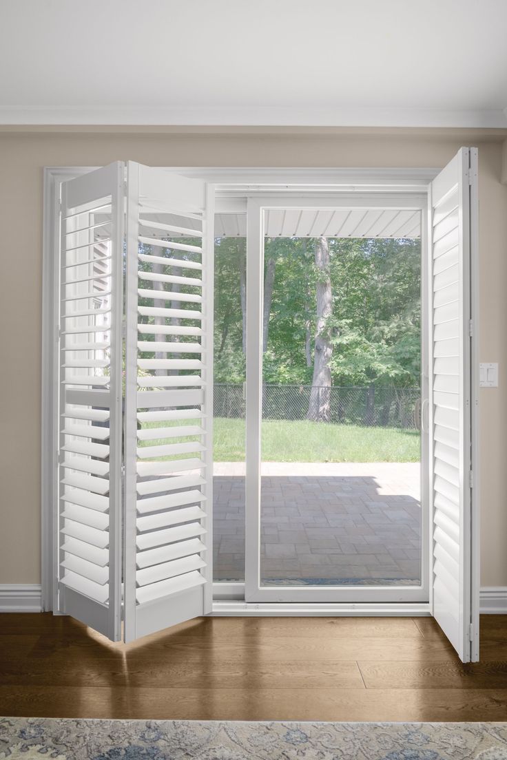White folding plantation shutters on a glass patio door with garden view, hardwood floor