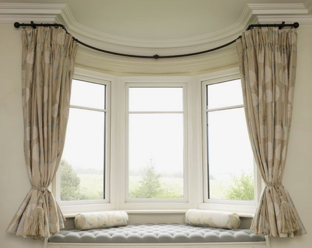 Elegant bay window with patterned blackout curtains, curved curtain track, and tufted bench seat