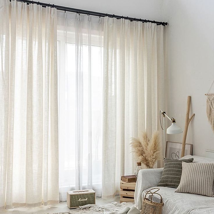 Sheer beige curtains on a large window in a cozy, minimalist living room with neutral decor.