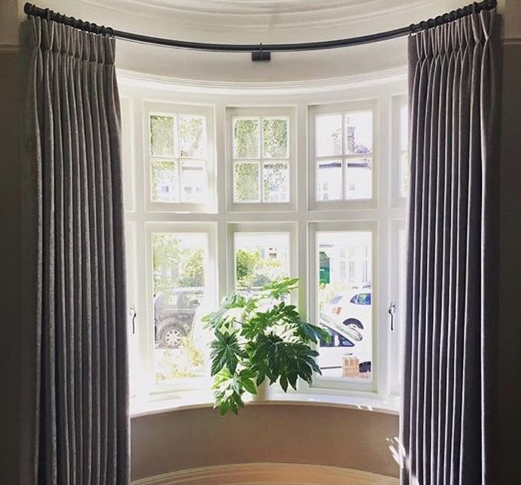 Bay window with pleated blackout curtains, white curtain track, and indoor plant.