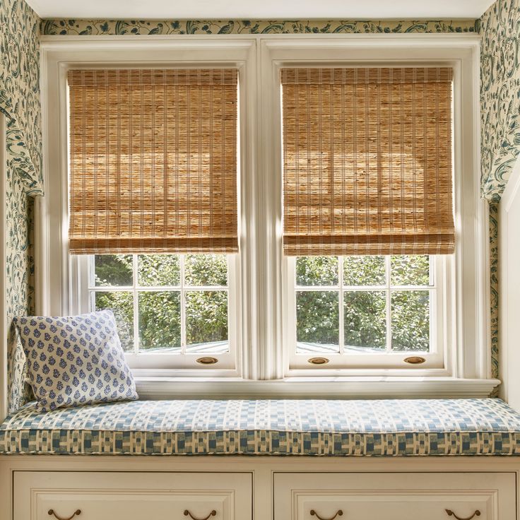 Cozy window seat with patterned cushion and pillow, double windows with woven bamboo blinds