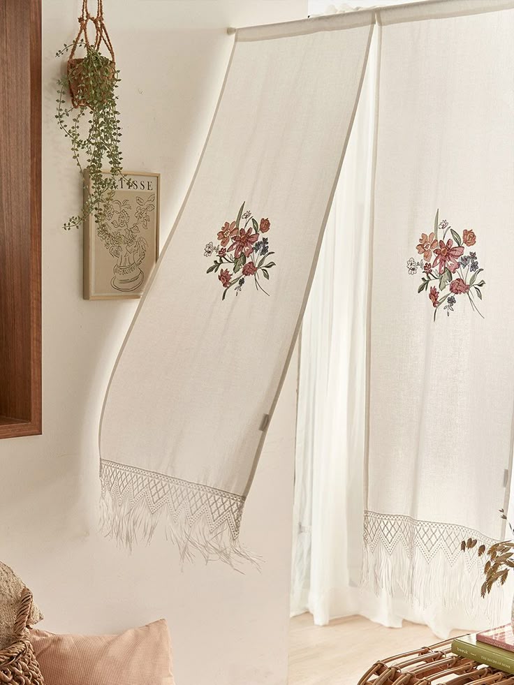 Sheer white curtain panels with floral embroidery and fringe, hanging in a cozy living room.