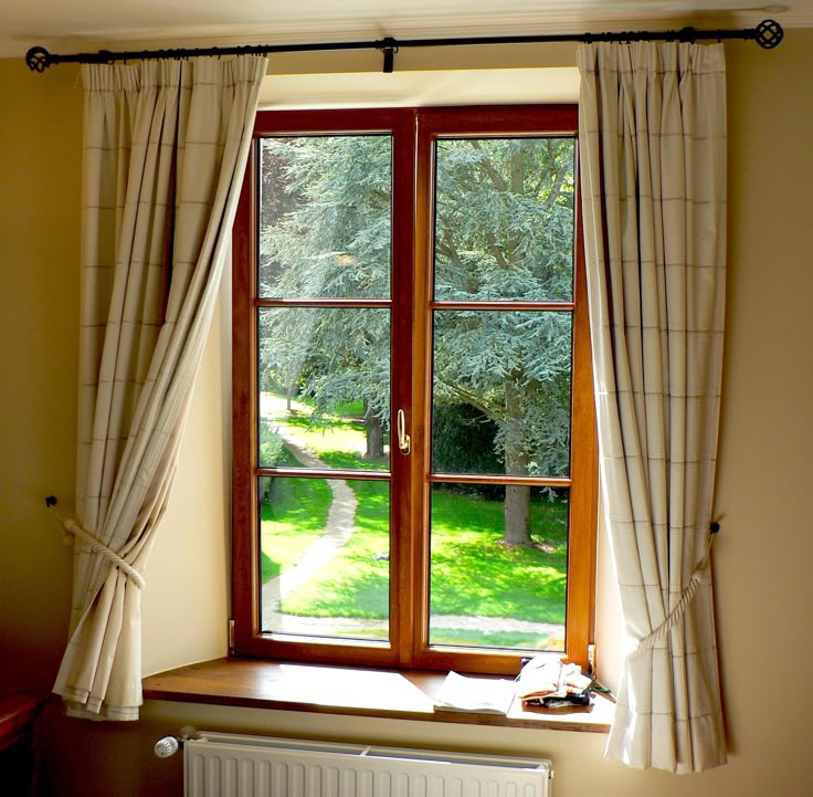Sunlit window with beige blackout curtains tied open, showing green garden view.
