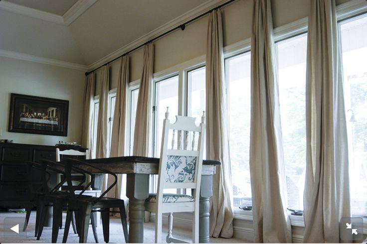 Dining room with long beige blackout curtains on large windows, wooden table and chairs