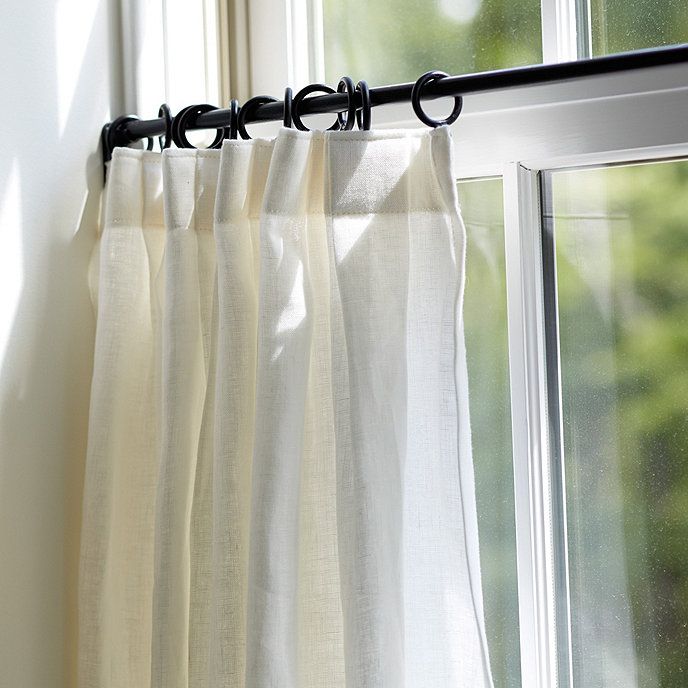 Sheer white curtain panel on black curtain rod, natural light streaming through window.