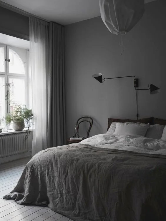 Modern bedroom with sheer blackout curtains, a large bed, grey walls, and soft natural lighting.