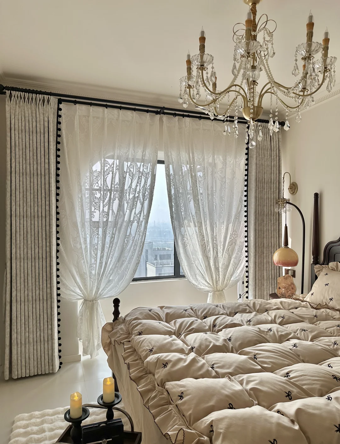 Luxurious bedroom with pleated blackout curtains, sheer lace panels, chandelier, and cozy bedding.