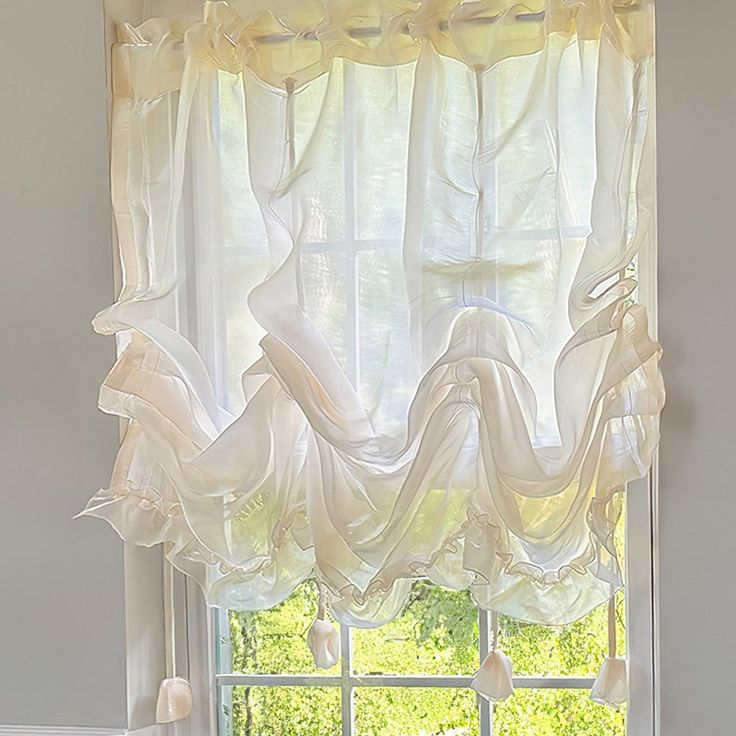 Sheer white ruffled curtain hanging on a sunlit window, creating an airy, elegant look.