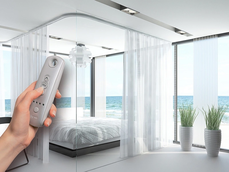 Hand holding remote to control sheer curtain track in modern bedroom with ocean view windows