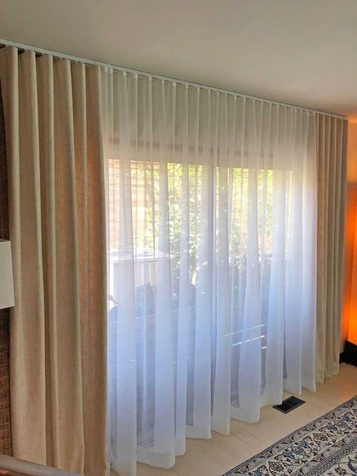 Ceiling-mounted beige blackout curtain with sheer white panel in a bright living room