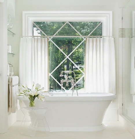 Modern bathroom with white blackout curtains, freestanding tub, and large window.