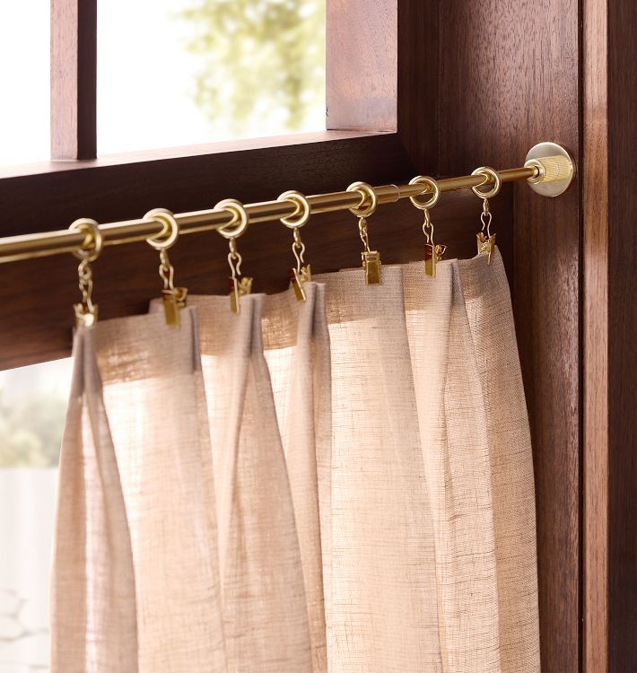 Sheer beige curtains on a gold curtain rod with rings in a wooden window frame