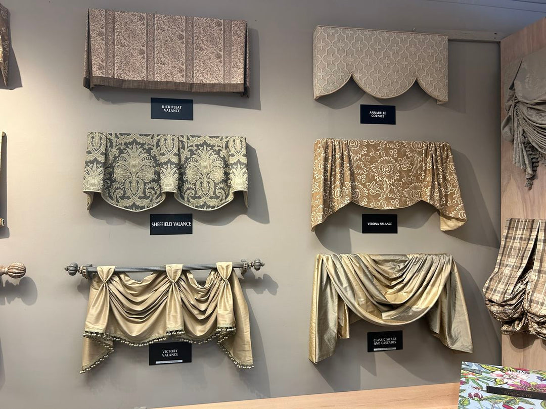 Display of various window valances in different fabrics and styles on a wall