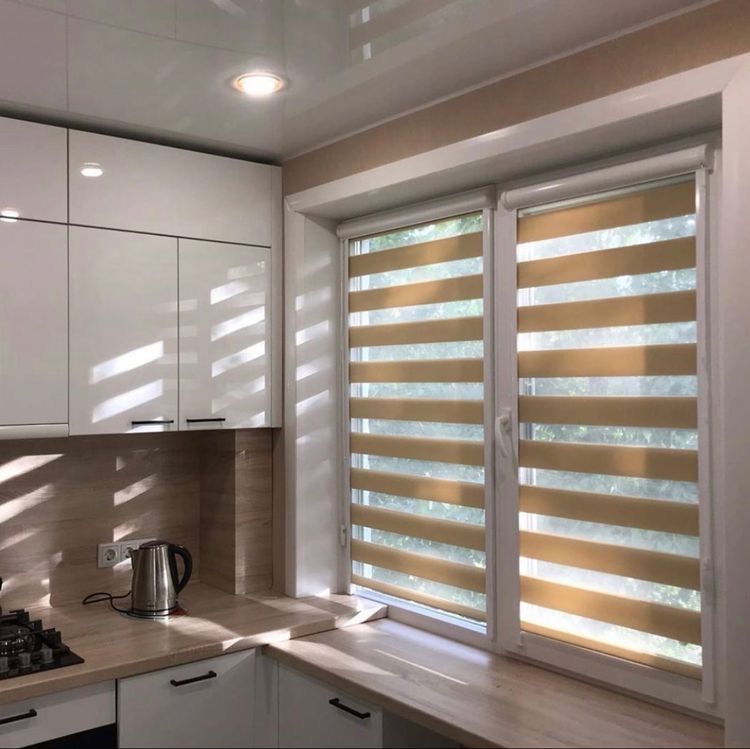 Modern kitchen with dual-layer zebra blinds, white cabinets, wood countertop, and sunlight filtering through.