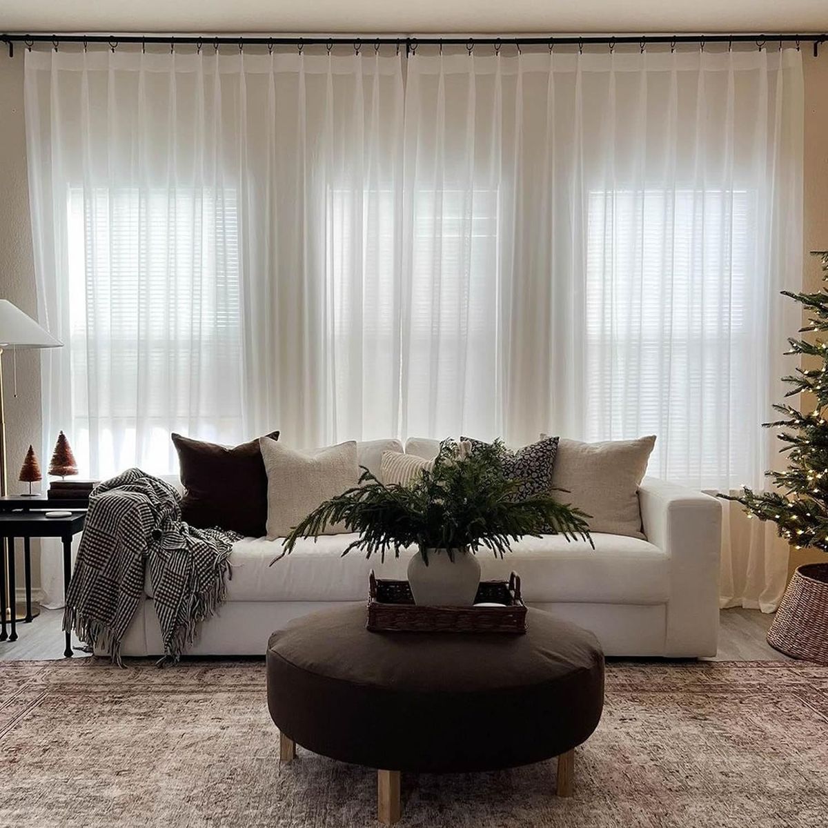 Modern living room with sheer white curtains, white sofa, and festive holiday decor