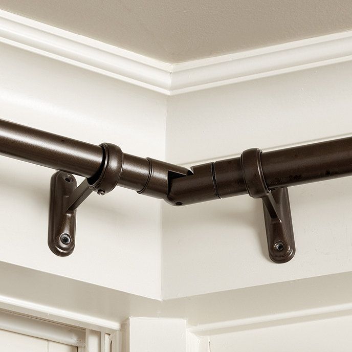 Dark metal corner curtain rod with wall brackets mounted on a white wall for window treatment