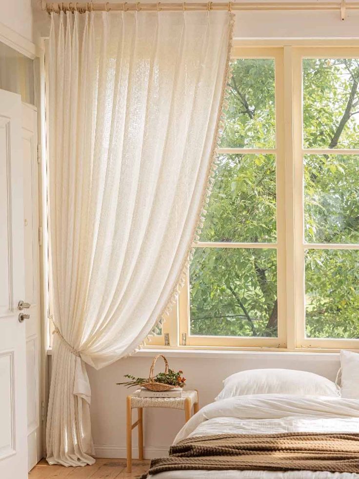 Elegant bedroom with soft beige curtains framing large windows, sunlight filtering through