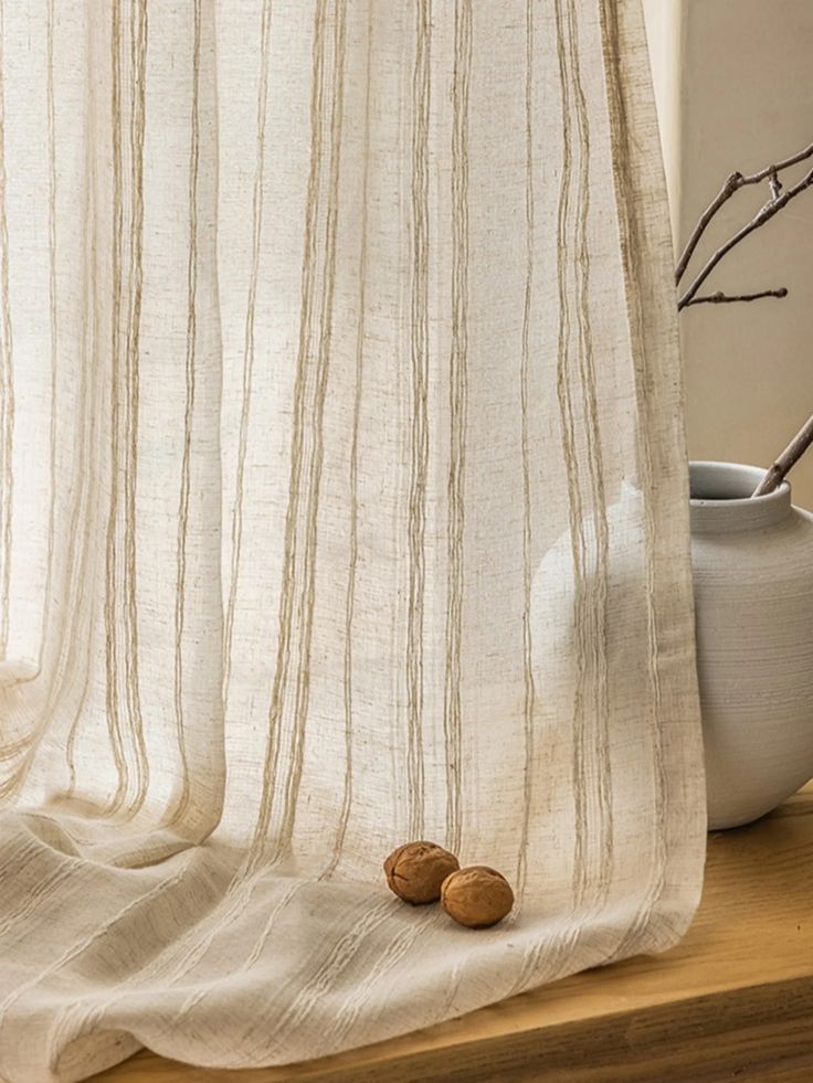 Beige sheer curtain with vertical stripes, walnuts, and ceramic vase on a wooden windowsill