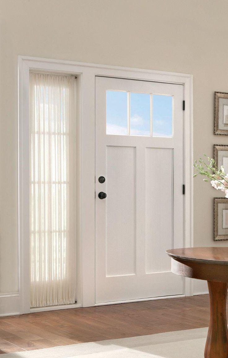White front door with transom windows and sheer side panel curtain on hardwood floor