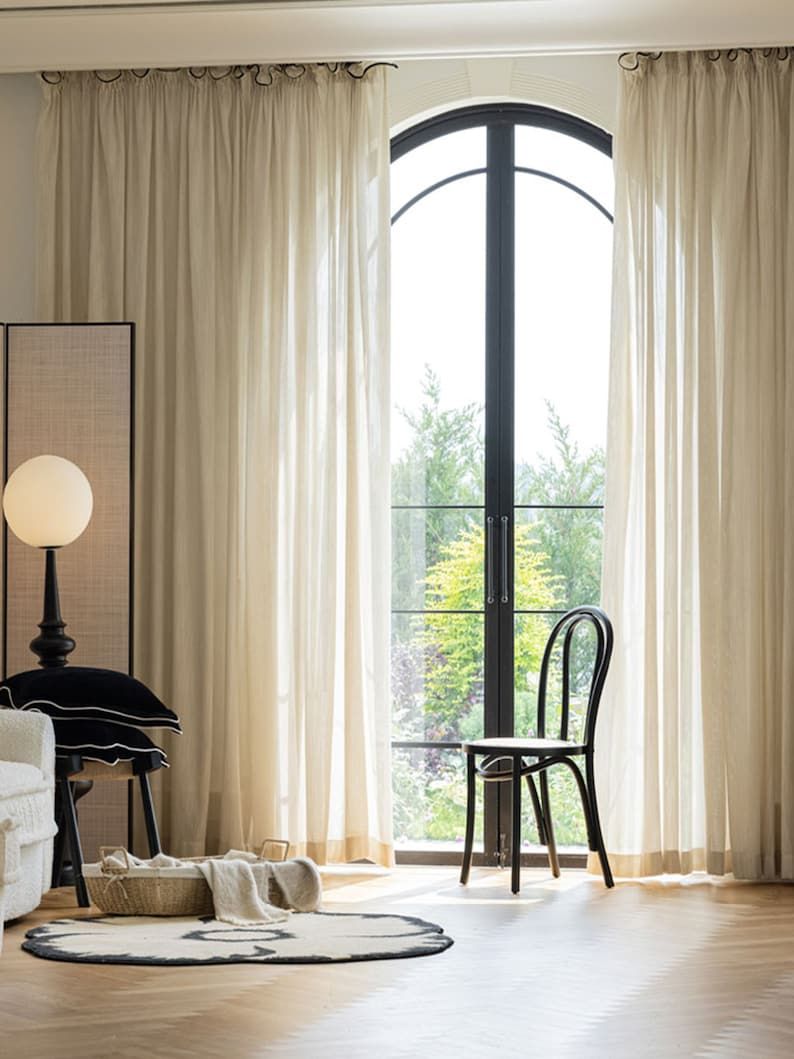 Elegant beige blackout curtains on arched window in modern living room with chair and soft rug