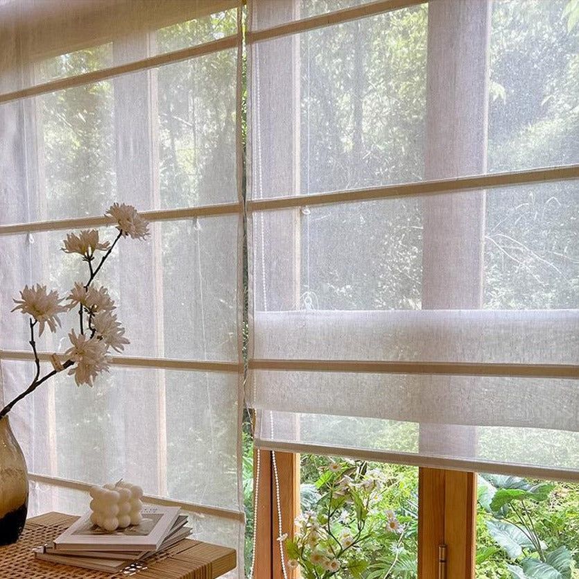 Light-filtering sheer roman curtains on wood frame window, table with vase and flowers