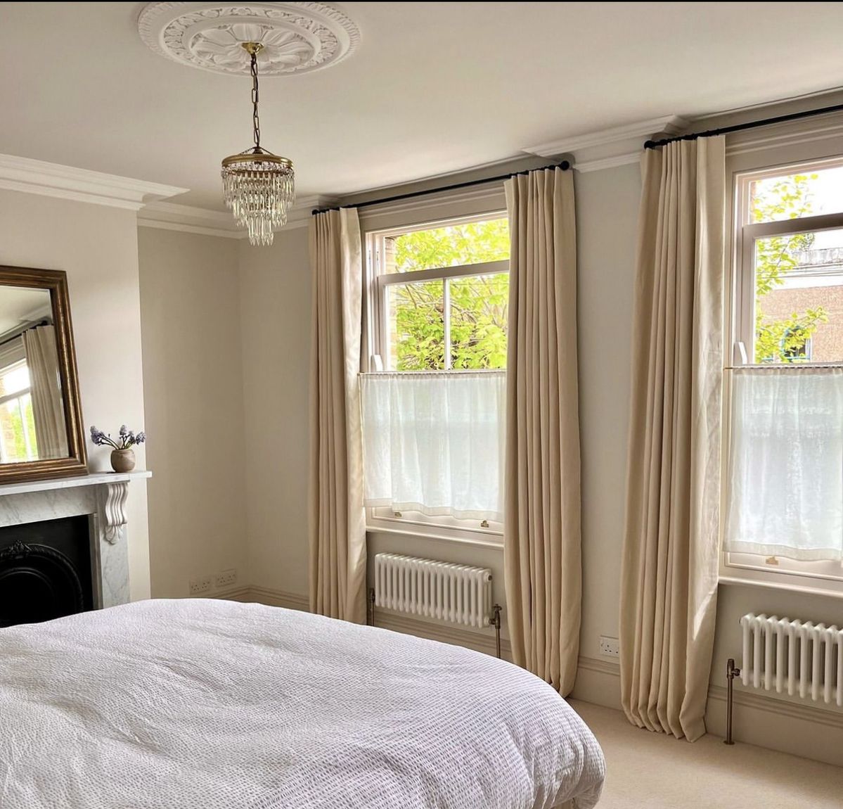 Bright bedroom with beige blackout curtains and sheer panels on tall windows, elegant decor