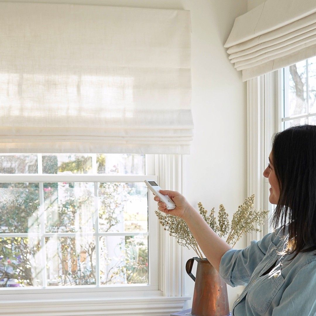 Woman using remote control to adjust modern white roman shades in bright living room