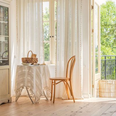 Bright room with sheer curtain panels, round table, wooden chair, and outdoor view