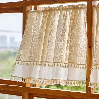Sheer lace curtain panel with tassel trim on wooden window, natural light filtering in