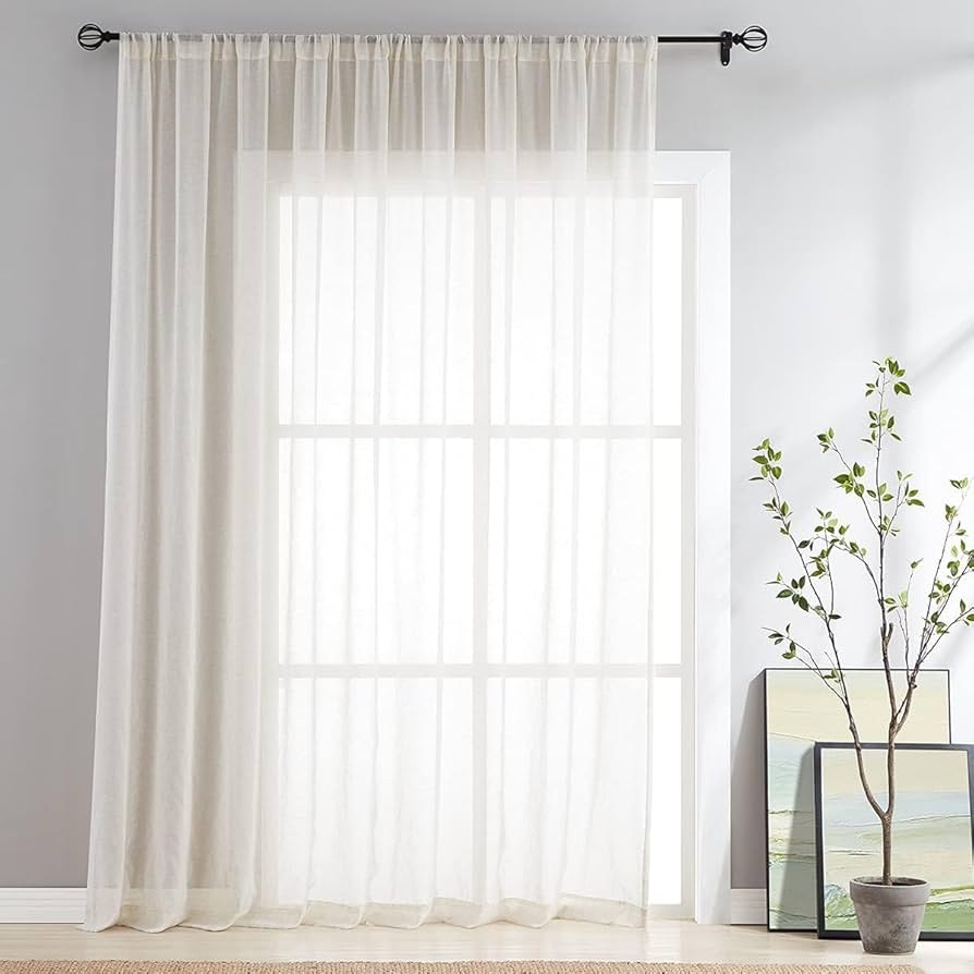 Sheer white curtain on a window with modern black curtain rod, potted plant, and wall art