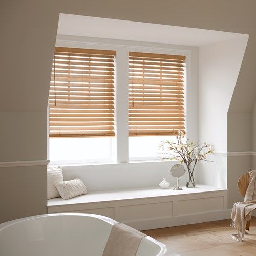 Bright modern bedroom with light wood blinds, window bench, pillows, and minimalist decor.