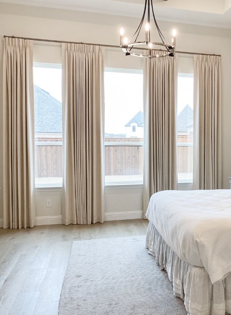 Modern bedroom with beige blackout curtains, floor-to-ceiling windows, and chandelier