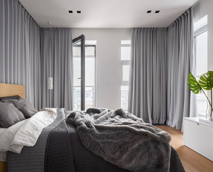 Modern bedroom with floor-to-ceiling gray blackout curtains, cozy bed, and natural light.